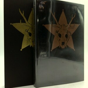 May include: Two black hardcover books with gold and brown star-shaped designs featuring a skull with antlers. The books are side-by-side.