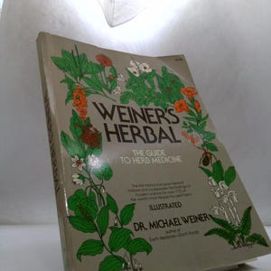 May include: A softcover book titled Weiner's Herbal: The Guide to Herb Medicine by Dr. Michael Weiner. The beige cover features a detailed botanical illustration of various green plants with orange and white flowers surrounding the black text.