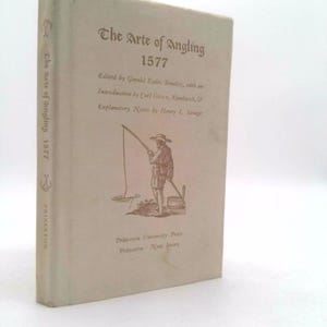 May include: A vintage book titled "The Arte of Angling 1577" with a cream-colored cover. The cover features text and an illustration of a person fishing. The book is published by Princeton University Press.