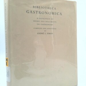 May include: A hardcover book titled "Bibliotheca Gastronomica" with text in black. The book's cover is a light beige color. The text on the cover includes "A Catalogue of Books and Documents on Gastronomy" and the author's name, André L. Simon.