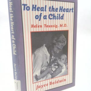 May include: A hardcover book titled "To Heal the Heart of a Child" by Helen Taussig, M.D. The cover features a black and white photo of a doctor examining a baby, with red and white striped background.