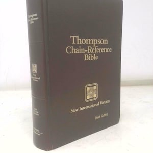 May include: A dark brown Thompson Chain-Reference Bible. The book has gold lettering on the cover that reads "Thompson Chain-Reference Bible" and "New International Version". The spine has the text "Thompson-Reference Bible".