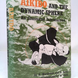 May include: Book cover with a green background and a black and white illustration of three people practicing Aikido. The title of the book is "Aikido and the Dynamic Sphere: An Illustrated Introduction" by A. Westbrook and O. Ratti. The book cover also includes the text "illustrations by O. Ratti".