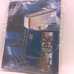 May include: A blue and black NASCAR souvenir program and a chrome-colored metal object are sealed in a clear plastic bag. The program features the text "BRICKYARD 400" and images of race cars. The NASCAR logo is visible.
