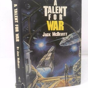 May include: A black paperback book with a cover featuring a futuristic spaceship in space. The title of the book is "A Talent for War" by Jack McDevitt.