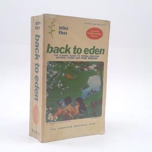 May include: A beige paperback book titled Back to Eden by Jethro Kloss. The cover features a green illustration of a landscape with two figures, a stream, and deer. Text includes The Classic Guide to Herbal Medicine, Natural Foods and Home Remedies.