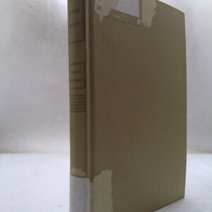 May include: A beige hardcover book standing upright, showing its spine and front cover. The spine features the text "Ripley Under Ground" and "Patricia Highsmith". There are white rectangular paper labels attached to the top and bottom of the spine.