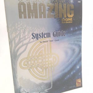 May include: A rule booklet titled "AMAZING ENGINE System Guide" by David "Zeb" Cook. The cover features gold lettering and a gold Celtic knot design. The background shows a tree, a person, and a starry sky.