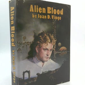 May include: A hardcover book titled "Alien Blood" by Joan D. Vinge. The cover features a portrait of a person with curly blonde hair and a white shirt. The background is dark with a futuristic design.