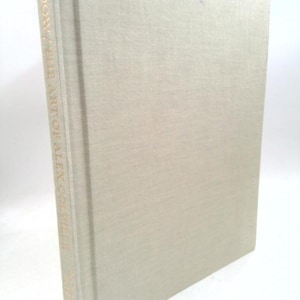 May include: A hardcover book titled "Dow / The Art of Alex Colville" with a light beige linen cover. The book's spine features gold lettering. The book is slightly angled, showcasing its cover and spine.