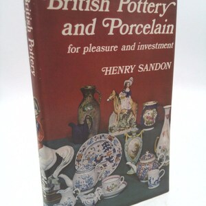 May include: A book titled "British Pottery and Porcelain for pleasure and investment" by Henry Sandon. The cover features a colorful illustration of various pieces of pottery and porcelain, including teapots, cups, plates, and figurines.