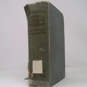 May include: A vintage book titled "Georgia Historical and Industrial" with a faded green cover. The book's spine displays the title in white lettering. A small white label is affixed to the spine. The book is slightly worn.