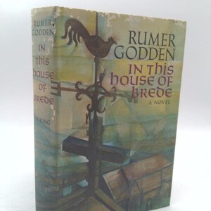 May include: A vintage hardcover book titled "In This House of Brede" by Rumer Godden. The cover features a weather vane illustration and a muted color palette of greens, blues, and browns. The book is published by Viking.