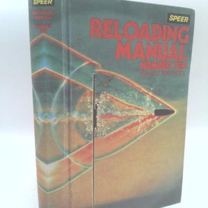 May include: A hardcover Speer Reloading Manual Number Ten for rifle and pistol. The dark green cover features a graphic illustration of a bullet in flight with red and yellow shockwave patterns and the title printed in bold red and yellow text.