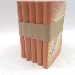 May include: A rectangular container made of stacked, orange-colored, cylindrical objects, bound by a brown paper band. The side of the container has a yellow and orange design with text. The container is on a white surface.