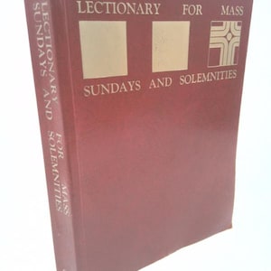 May include: A maroon book titled "Lectionary for Mass Sundays and Solemnities." The cover features gold lettering and a gold cross symbol. The spine also has the title in gold lettering. The book is set against a white background.
