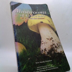 May include: A book titled "Mushrooms of Colorado" with a colorful mushroom illustration on the cover. The cover features text, including the author's name, and mentions the Southern Rocky Mountains. The book is published in cooperation with the Denver Botanic Gardens and Denver Museum of Natural History.