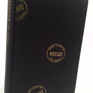 May include: A hardcover book with a black cover and gold lettering and circular stamps. The book's spine reads "WEEGEE BY WEEGEE" vertically. The cover features the text "CREDIT PHOTO BY WEEGEE THE FAMOUS" in gold.