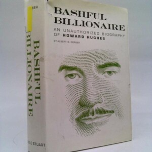 May include: A white book with a green and white illustration of a man's face on the cover. The title of the book is "Bashful Billionaire: An Unauthorized Biography of Howard Hughes" by Albert B. Gerber.