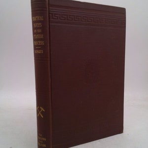 May include: A burgundy hardcover book titled "Practical Notes on the Cyanide Process" by Bosqui. The book has a gold Greek key design at the top and a gold pickaxe symbol on the side. The book is published by The Engineering and Mining Journal.