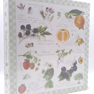 May include: A rectangular box with a botanical design featuring illustrations of fruits and flowers, including blackberries, strawberries, and oranges. The design is set against a white background with handwritten text and a light green checkered border.