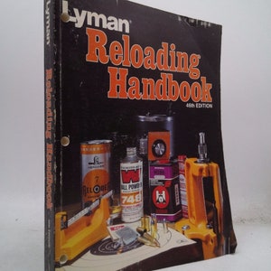May include: A black and orange book titled "Lyman Reloading Handbook 46th Edition". The cover features a still life of reloading supplies, including a scale, powder, bullets, and a reloading press.