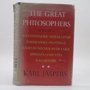 May include: A hardcover book titled The Great Philosophers Volume II by Karl Jaspers with a red dust jacket. The cover features white text listing philosophers including Anaximander, Heraclitus, Parmenides, Plotinus, Anselm, Nicholas of Cusa, Spinoza, Lao-Tzu, and Nagarjuna.