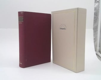 May include: A maroon hardcover book with a dark spine label and a cream-colored slipcase. The slipcase features a small logo with the text The Library of America and an open book icon centered on the front panel, with a thin gold border.