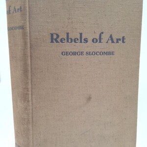 May include: A tan linen-bound book with the title "Rebels of Art" and the author's name "George Slocumbe" printed in dark blue ink.