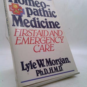May include: A hardcover book titled "Homeopathic Medicine" with the subtitle "First-Aid and Emergency Care." The cover features the title in blue and red text, with the author's name, Lyle W. Morgan, at the bottom.