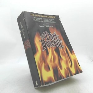 May include: A hardcover book titled The Dark Descent, edited by David G. Hartwell. The black cover features a graphic of yellow and orange flames. The text includes The Evolution of Horror and names of authors like Clive Barker and Ray Bradbury.