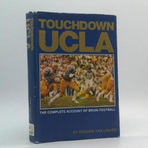 May include: A blue book titled "Touchdown UCLA" with gold lettering. The cover features a football game scene with players in yellow and blue uniforms. The text "The Complete Account of Bruin Football" is also visible.
