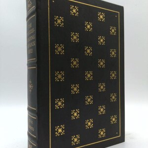 May include: A black hardcover book with gold foil stamping. The front cover features a repeating pattern of small gold star-like ornaments within a thin gold border. The spine displays the title The Puzzle of the Reading Stock Rifle and author.