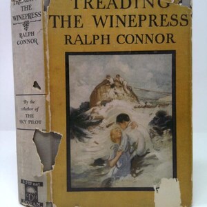 May include: A vintage book titled "Treading the Winepress" by Ralph Connor. The cover is yellow with black text and a framed illustration of people in water. The spine is off-white with text and a grape illustration. The book shows signs of wear.