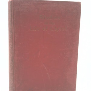 May include: A maroon-colored book with the title "Studies in the Life of Christ" in gold lettering. The book has a worn appearance, suggesting it is an antique or vintage item. The cover is a solid maroon color.