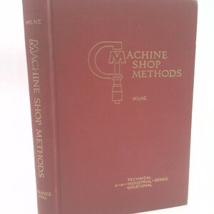 May include: A maroon-colored book titled "Machine Shop Methods" by Milne. The book's cover features a silver illustration of a machine shop tool and text. The spine also displays the title vertically.
