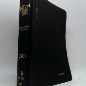 May include: A black "Nelson Study Bible" with gold lettering. The spine features the text "The Nelson Study Bible", "Nelson's Complete Study System", "NKJV", and "Nelson". The book is a hardcover edition with the name "James Olson" printed on the bottom right.