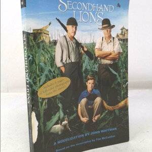 May include: A book cover for the novel "Secondhand Lions" by John Whitman. The cover features a photo of three people in a cornfield, with a dog in the foreground. The book is based on the screenplay by Tim McCanties.