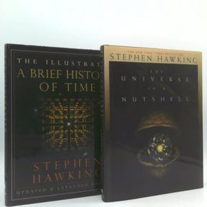 May include: Two hardcover books by Stephen Hawking. The book on the left is titled "The Illustrated A Brief History of Time." The book on the right is titled "The Universe in a Nutshell." Both books have dark covers with gold lettering.