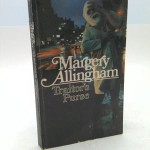 May include: A vintage hardcover book titled "Traitor's Purse" by Margery Allingham. The cover features a nighttime scene with a figure wearing a mask. The book's spine displays the author's name and title. The overall color scheme is dark with touches of orange and white.