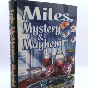 May include: A hardcover book titled Miles, Mystery & Mayhem by Lois McMaster Bujold. The cover features a dark table with a glass decanter, a wine glass, a small bowl, flowers, and a framed portrait. A futuristic weapon rests on the table surface.