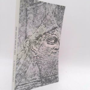 May include: A softcover book titled The Essene Book of Asha by Edmond Bordeaux Szekely. The cover features a black and white graphic illustration of an ancient profile portrait with a textured beard and a tall headdress on a light background.
