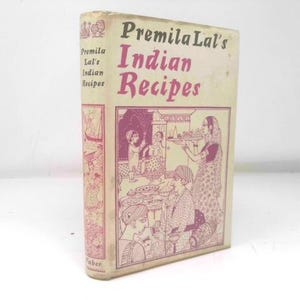 May include: Vintage cookbook titled "Premila Lal's Indian Recipes." The cover features a pink and white illustration of people in traditional Indian attire, with the title in a bold, pink font. The book is slightly worn, suggesting its age.