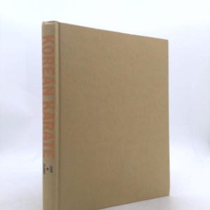 May include: A hardcover book with a tan cover. The spine features the text KOREAN KARATE in orange capital letters, with the author name CLARK and the name SON printed in smaller black text below the title on the spine of the book.