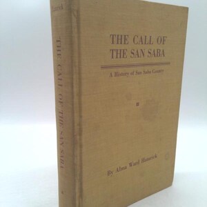 May include: A hardcover book titled "THE CALL OF THE SAN SABA" with text in purple. The book has a tan cover and spine. The author's name, Alma Ward Hamrick, is printed at the bottom. The book is a history of San Saba County.