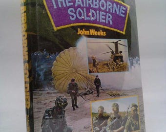 May include: A book titled "The Airborne Soldier" by John Weeks. The cover features a camouflage pattern and images of soldiers in action, including a helicopter, a parachute, and soldiers with rifles.