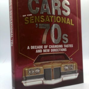 May include: A book titled "Cars of the Sensational 70s" with a red cover and gold lettering. The cover features a gold car illustration. The spine reads "Cars Sensational '70s". The book's subtitle is "A Decade of Changing Tastes and New Directions."