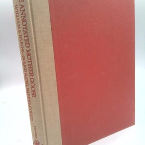 May include: A hardcover book titled "THE ANNOTATED MOTHER GOOSE" by William S. Baring-Gould & Ceil Baring-Gould. The book has a red cover and a beige spine with text. The book is slightly angled, showing the cover and spine.