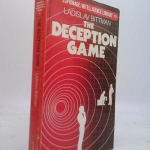 May include: A vintage book titled "The Deception Game" by Ladislav Bittman. The cover is red with white text and a graphic of concentric circles and silhouettes. The spine reads "The Deception Game" vertically.