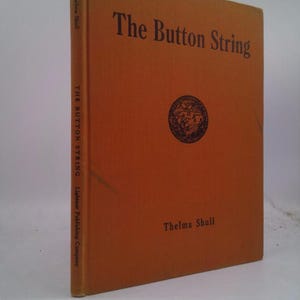 May include: An orange book with the title "The Button String" by Thelma Shull. The book cover features a small illustration of a globe.